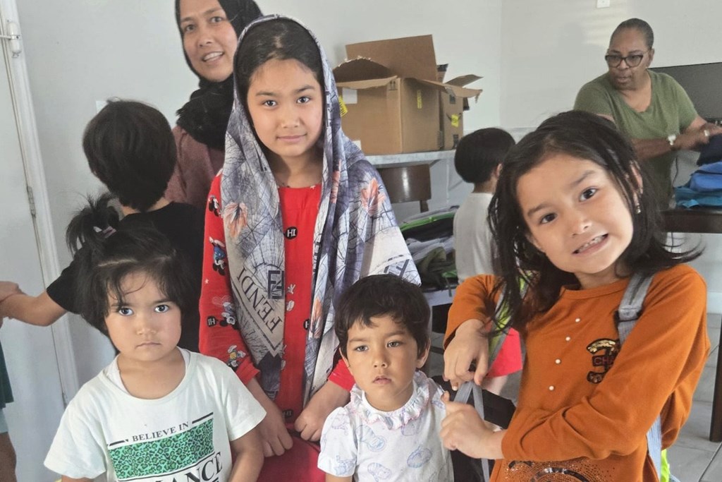 A woman and three children are standing in a room with boxes in the background.