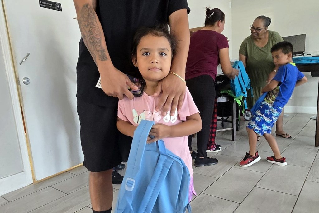 A little girl is holding a blue jacket while standing next to a man.