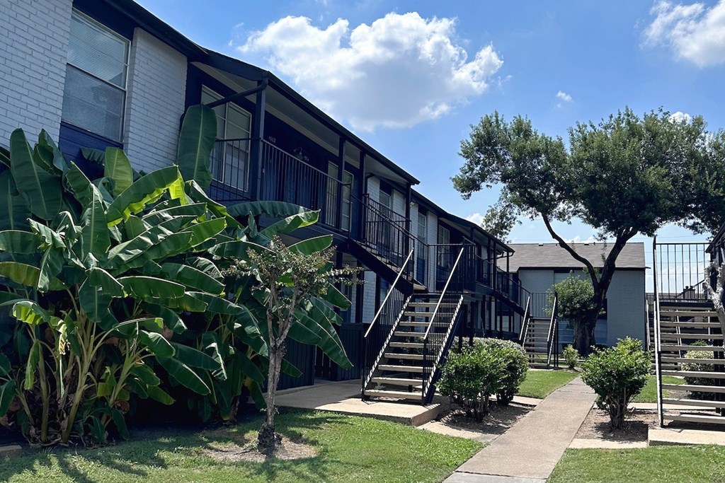 A tree is in front of a white building with a black railing.