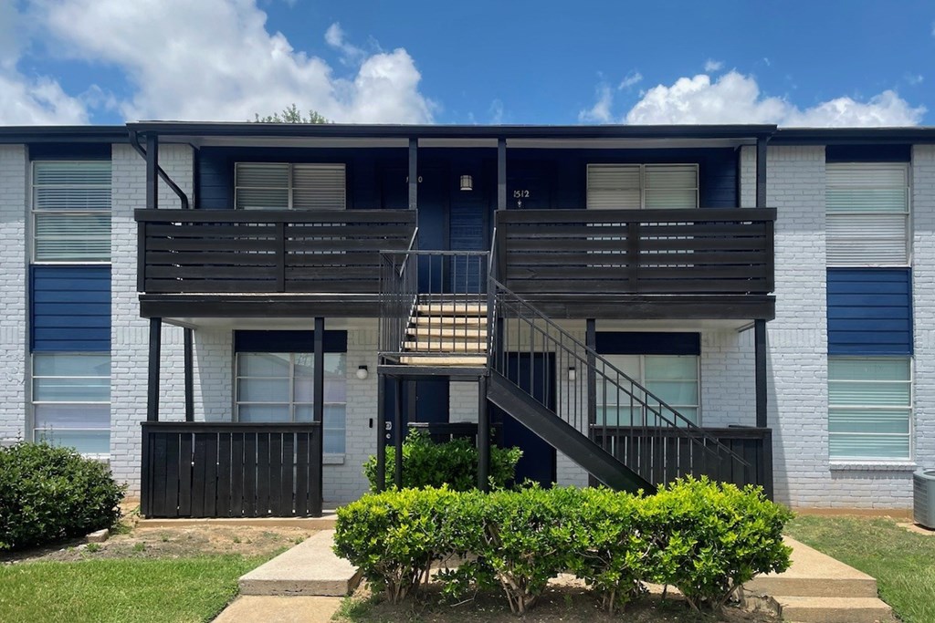 A two-story apartment building with a balcony and stairs.