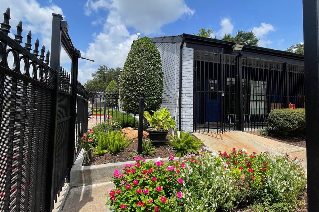 A black iron fence with a gate stands in front of a building with a black iron gate.