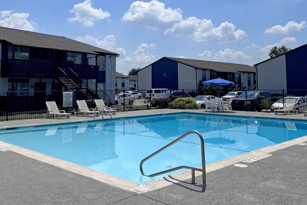 A swimming pool with a ladder in the foreground and apartment buildings in the background.