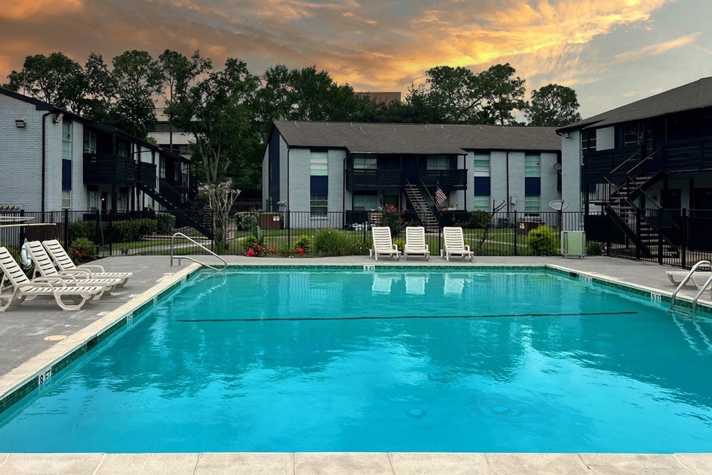 A swimming pool surrounded by lounge chairs and apartment buildings.