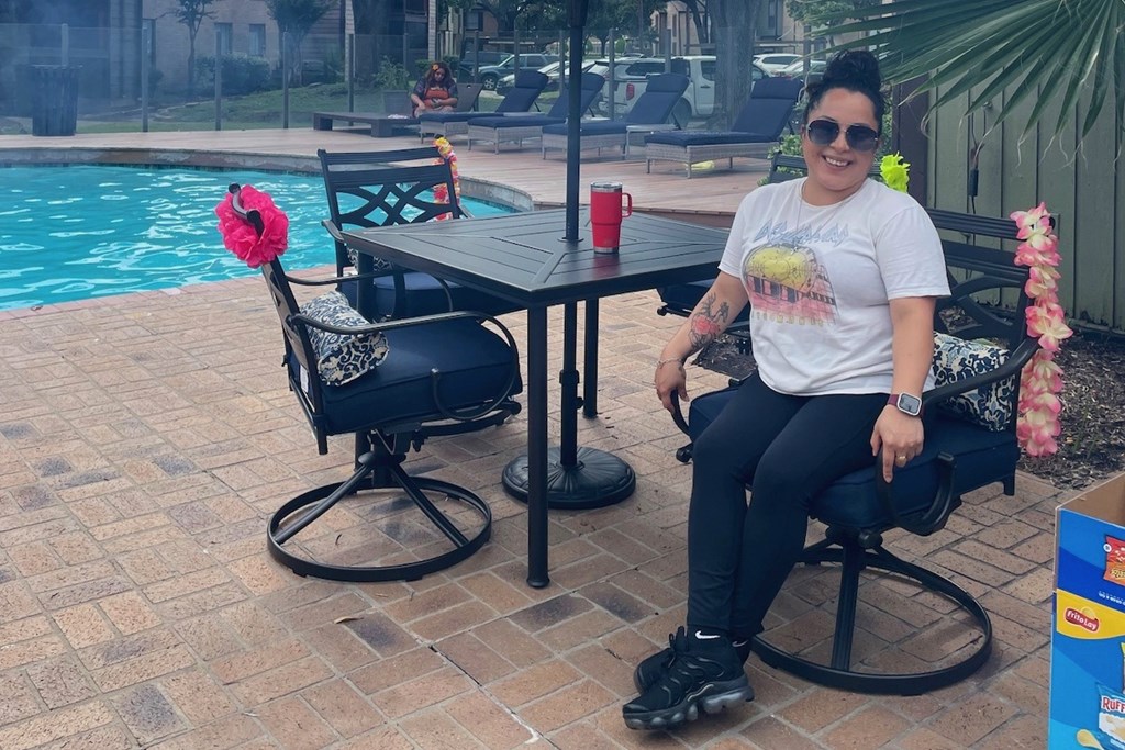 A woman sits at a table by a pool with a red cup on it.