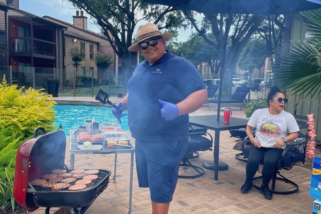 A man in a blue shirt and hat is grilling meat on a barbecue.