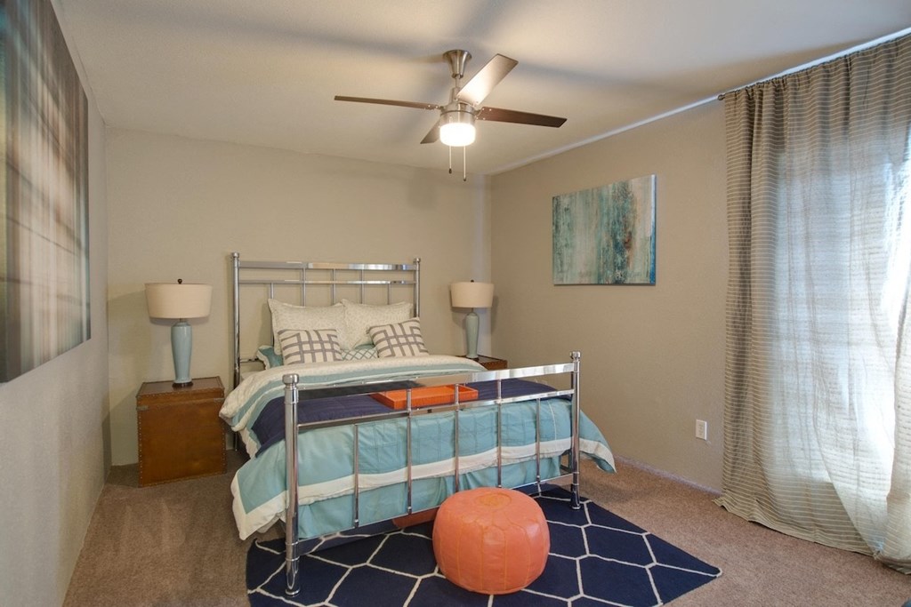 a bedroom with a bed and an illuminated ceiling fan, and large window behind a curtain