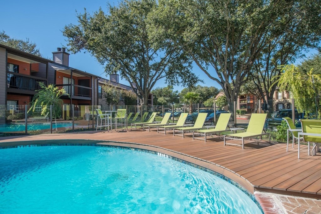 a crystal blue swimming pool surrounded by green lounge chairs and lush trees
