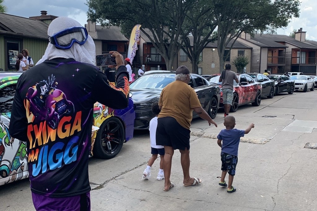 A person in a black shirt with colorful text is standing in front of a line of cars.