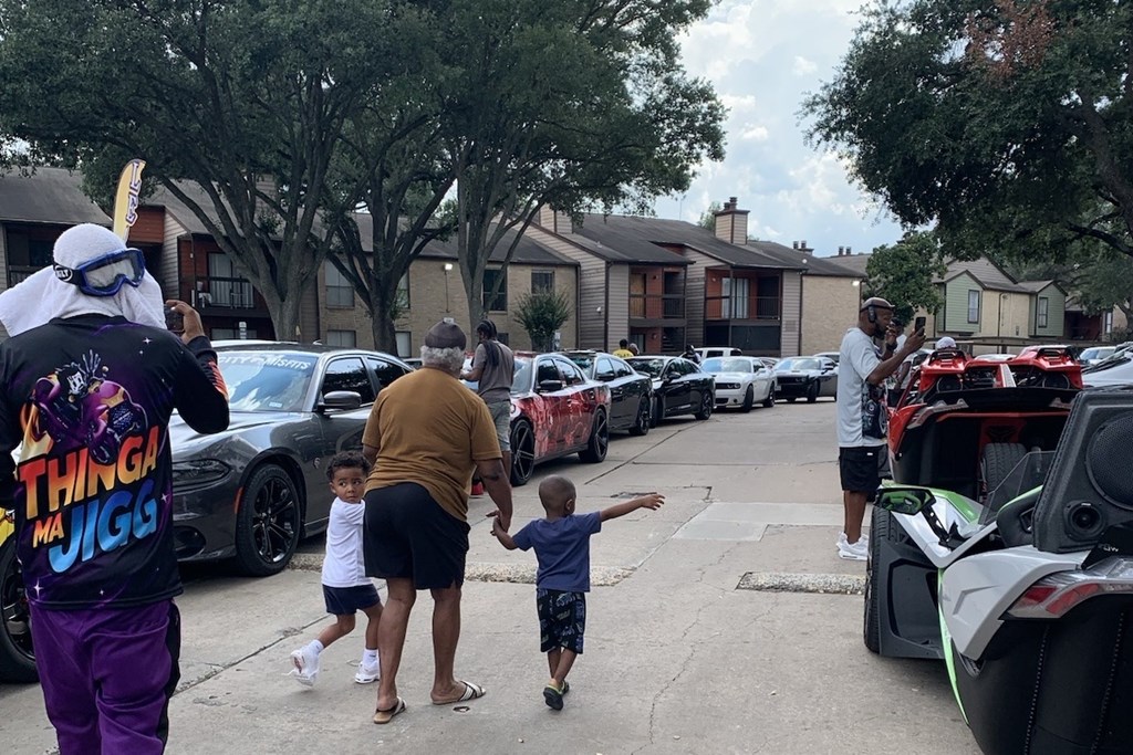 A man in a purple outfit is holding hands with a child while walking in a parking lot.
