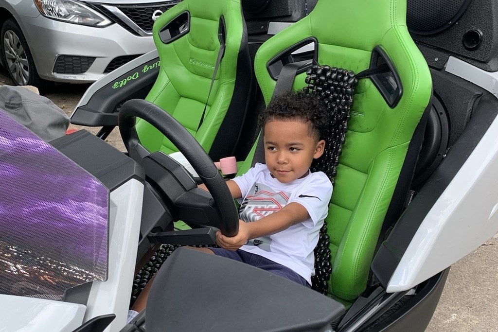 A young child is sitting in a green and black racing simulator.
