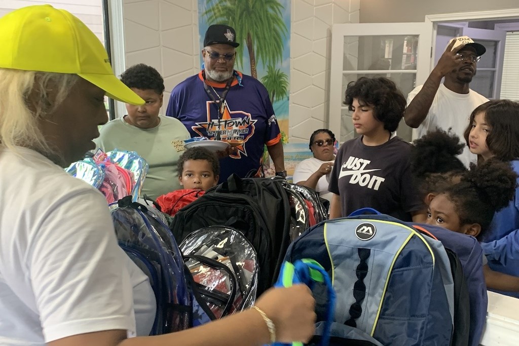 A group of people are gathered around a child in a red shirt.