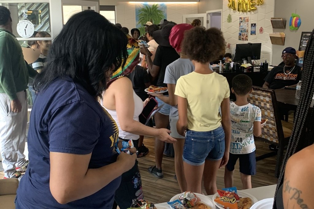 A group of people are gathered around a table in a room with a clock on the wall.