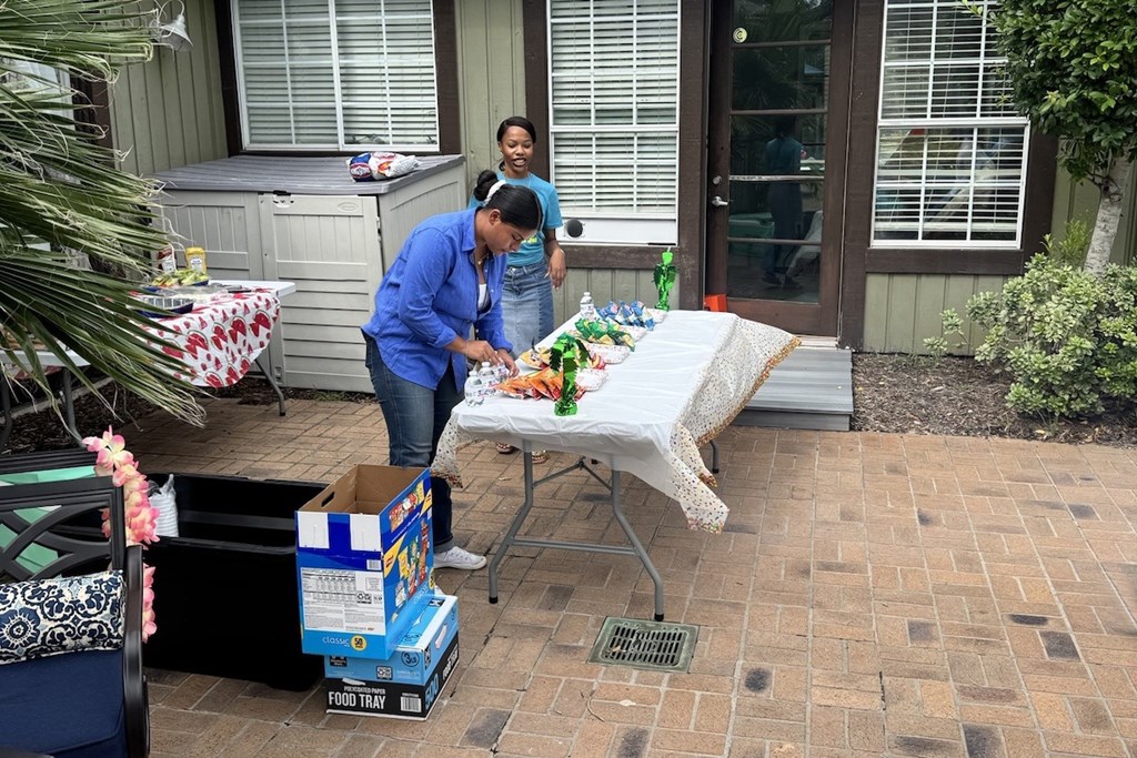 A woman in a blue shirt is setting a table outside.