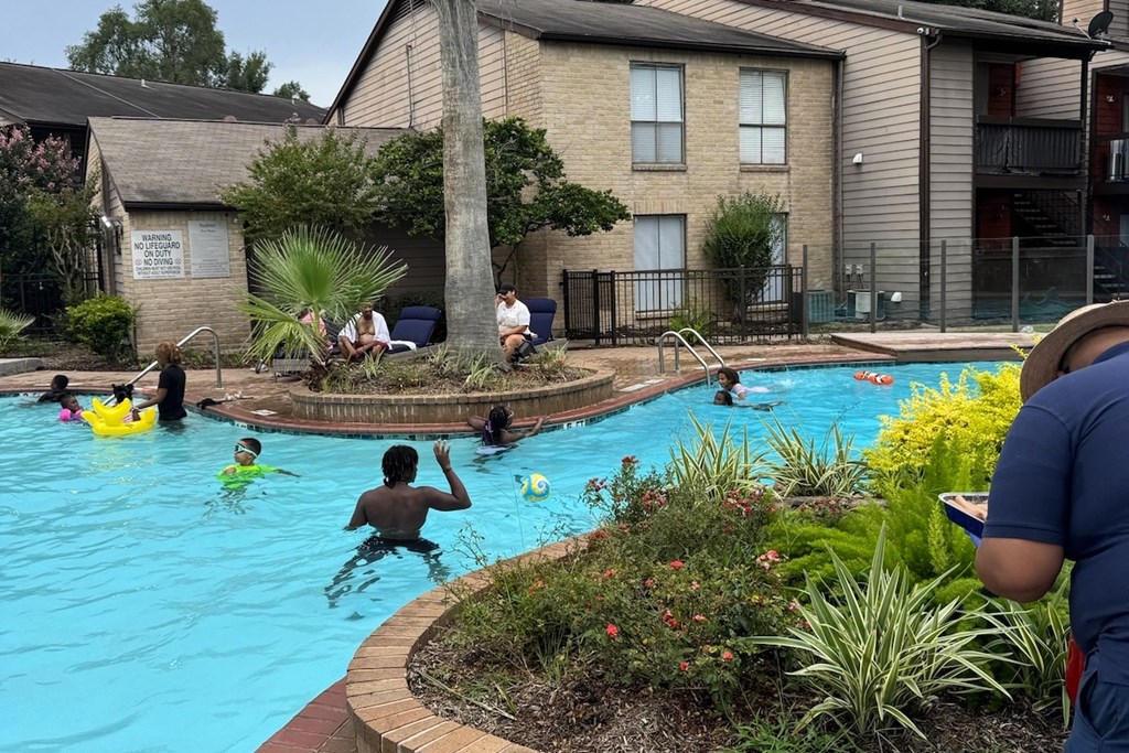 A man in a blue shirt is standing by a pool with children playing in it.