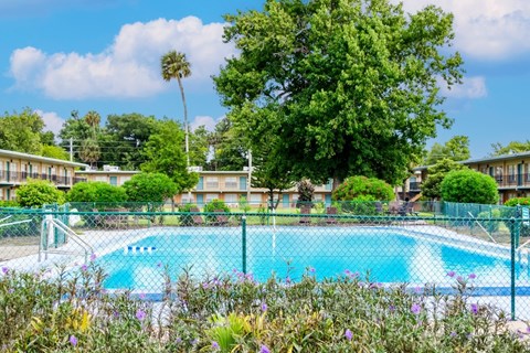 A pool surrounded by a green fence and trees.