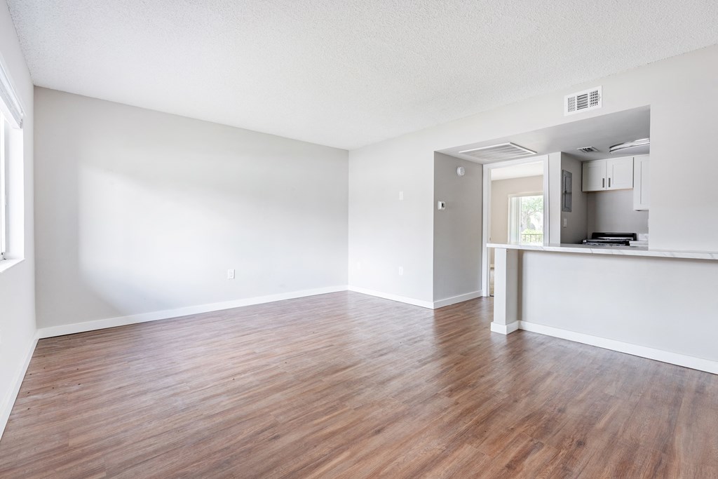 an empty living room with a kitchen in the background