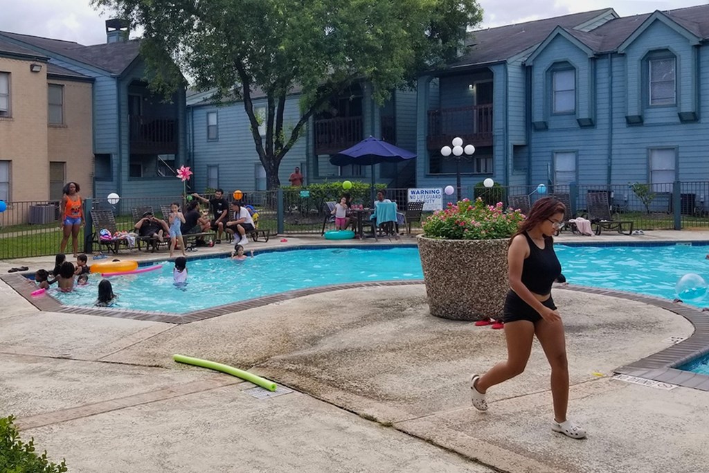 A woman is running by a pool with people swimming in it.
