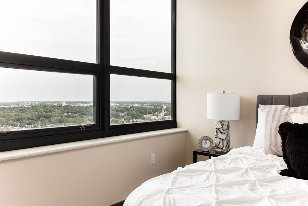 A bedroom with a large window overlooking a cityscape.