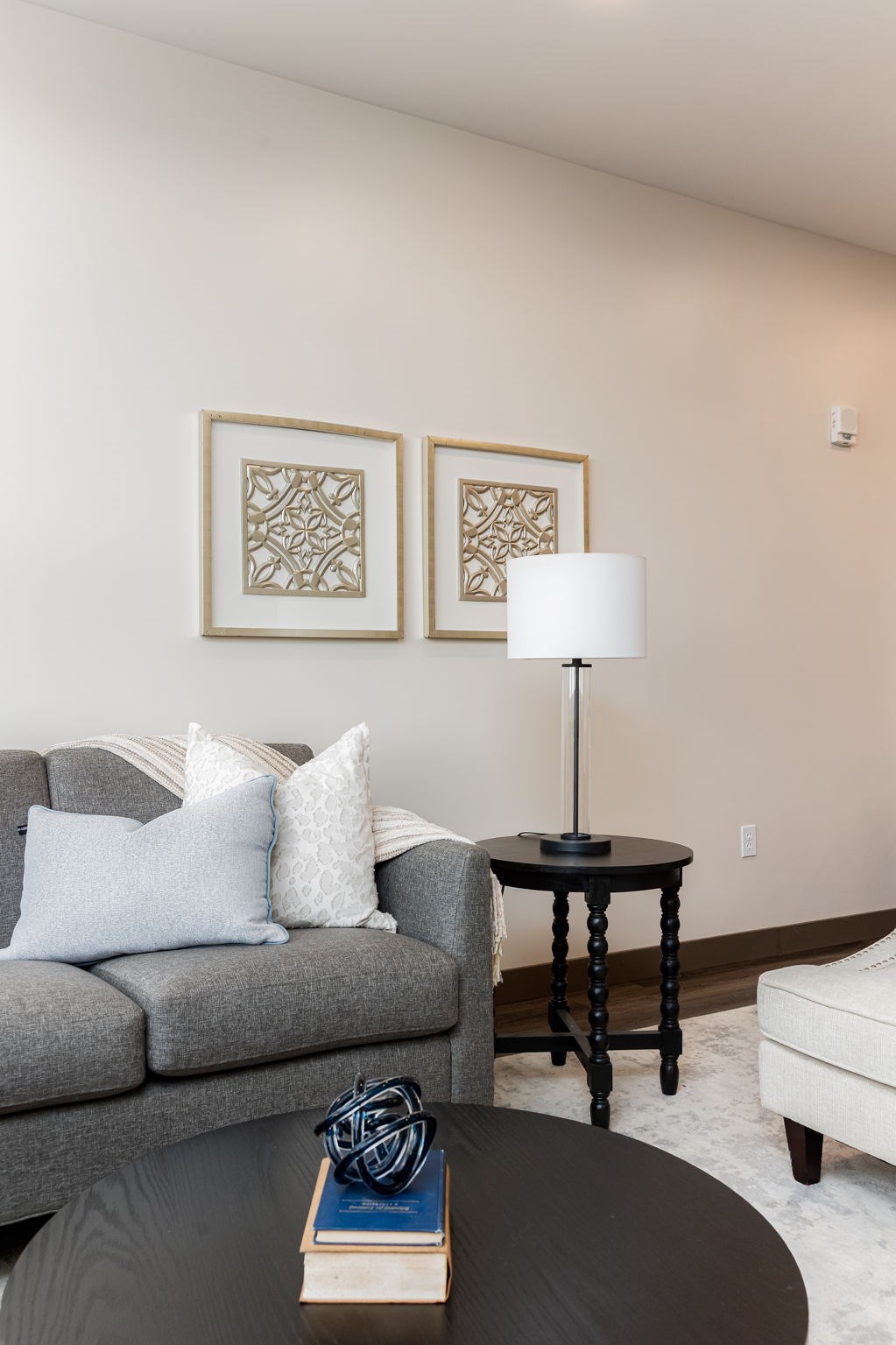 A living room with a grey couch, a black table, and two framed pictures on the wall.