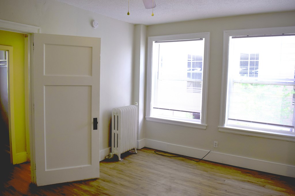 A room with a white door, two windows, and a radiator.