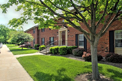 exterior view of a brick apartment building with a sidewalk and trees