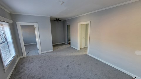 an empty living room with three doors and a ceiling fan