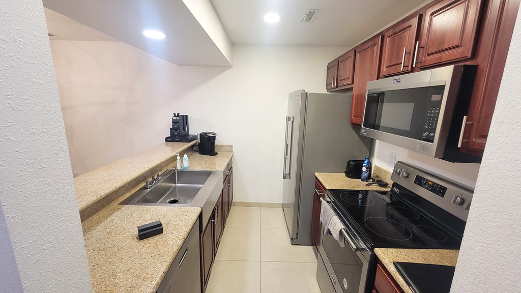 A kitchen with a refrigerator, microwave, oven, and sink.
