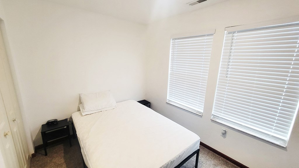 A bedroom with a bed, nightstand, and window with blinds.