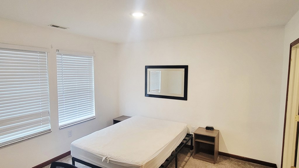 A bedroom with a bed, a mirror, and a window with blinds.