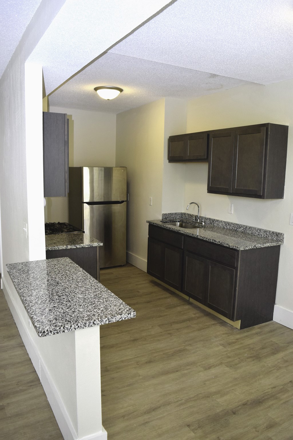 A kitchen with a granite counter top and dark brown cabinets.