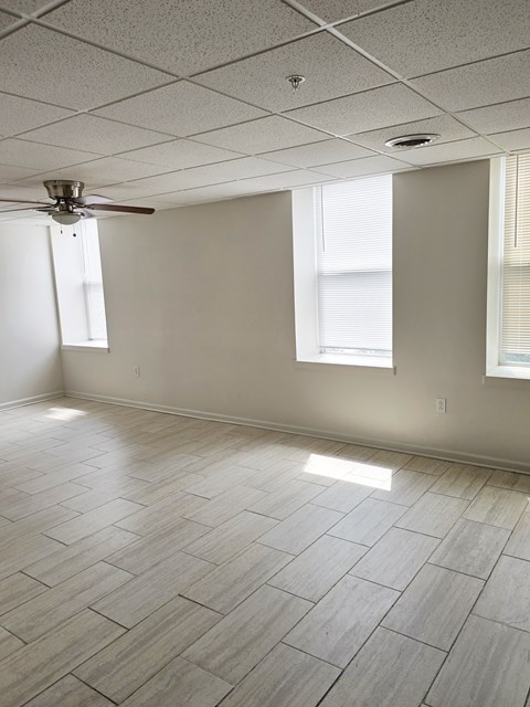 A room with a ceiling fan and light, tile flooring, and two windows.