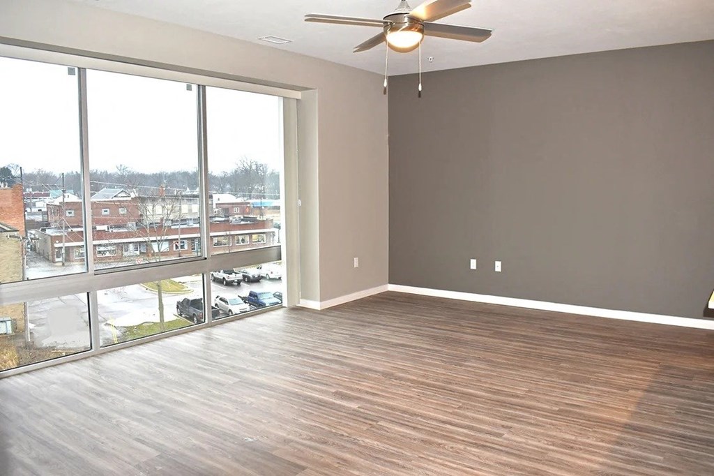 an empty living room with a large window and a ceiling fan