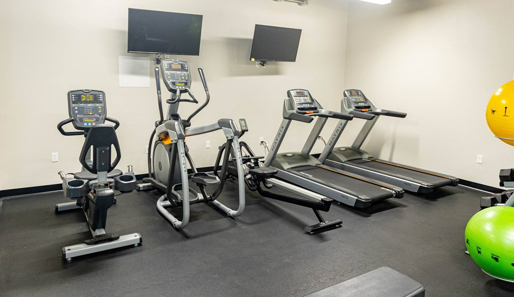 a gym with four ellipticals and a tv on the wall