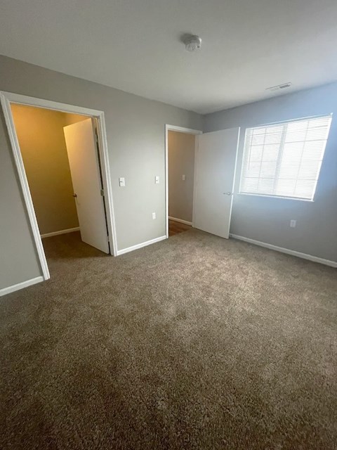 A room with carpeted floor and a window with blinds.