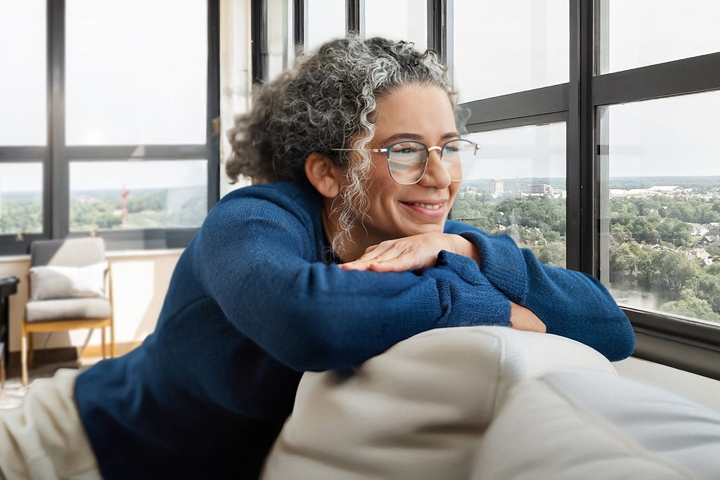 A person with curly hair wearing glasses and a blue top is sitting on a couch.