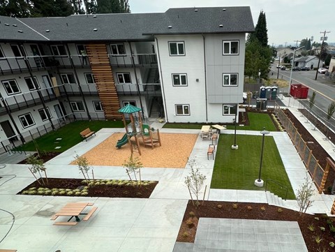A playground area with a slide and a green umbrella is surrounded by apartment buildings.