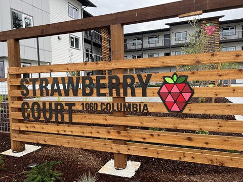 A wooden sign that says Strawberry Court in front of a building.