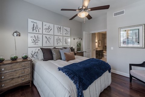 A bedroom with a bed, a ceiling fan, and a wall with pictures.