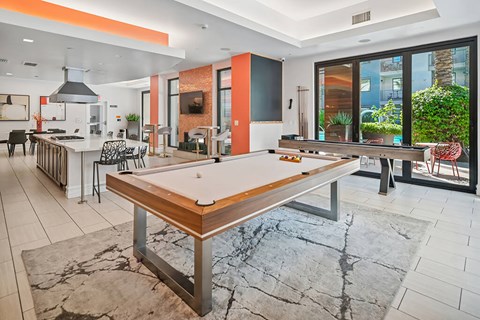 A billiard table is in the middle of a room with a kitchen area.