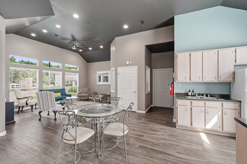 A kitchen with a table and chairs in the foreground and a living room with a couch and chairs in the background.