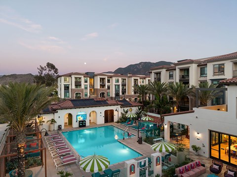 A large, luxurious pool surrounded by lounge chairs and umbrellas is the centerpiece of a resort-style complex.