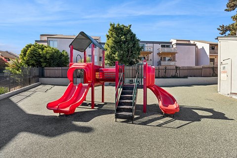 A red playground slide in the middle of a playground.