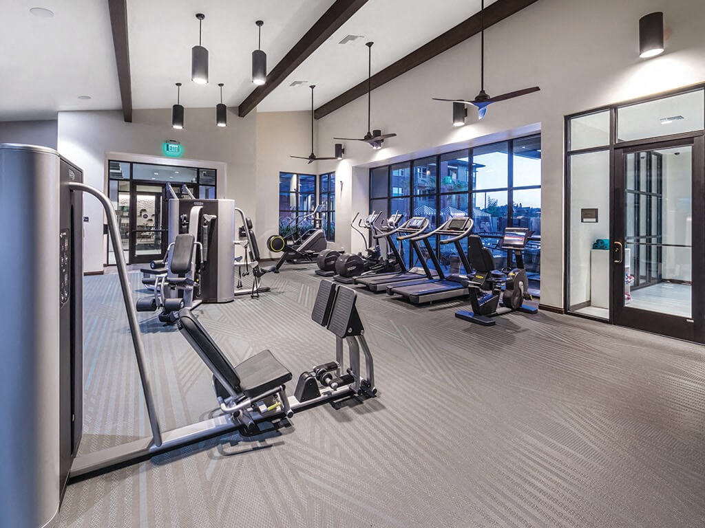 a spacious fitness center with cardio equipment and windows with views of the city