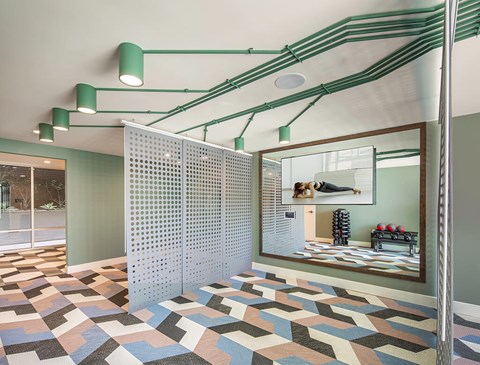 A room with a white perforated wall and a mirror reflecting a room with a bed and a dog.