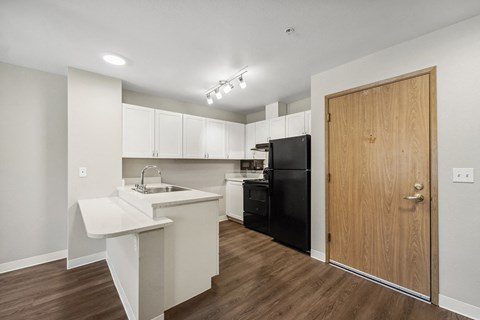 a white kitchen with a black refrigerator and a white counter top