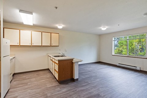 an empty living room with a kitchen and a window