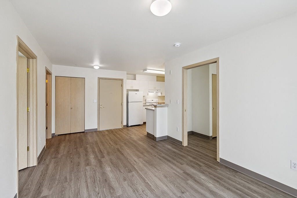 an empty living room with a kitchen in the background