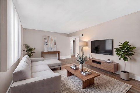 A living room with a white sofa, a wooden coffee table, and a flat-screen TV mounted on the wall.