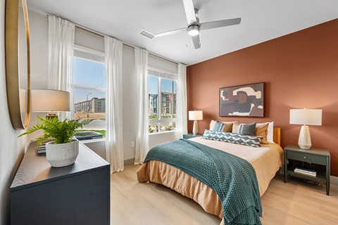 A bedroom with a bed, a ceiling fan, and a view of the city.