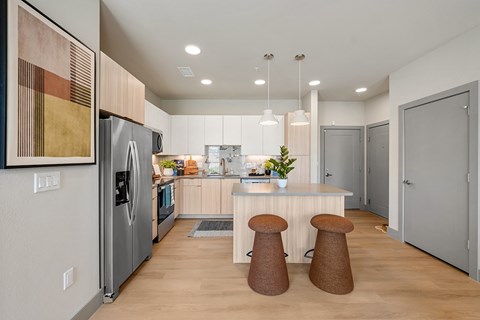 A kitchen with a refrigerator, stove, and bar stools.